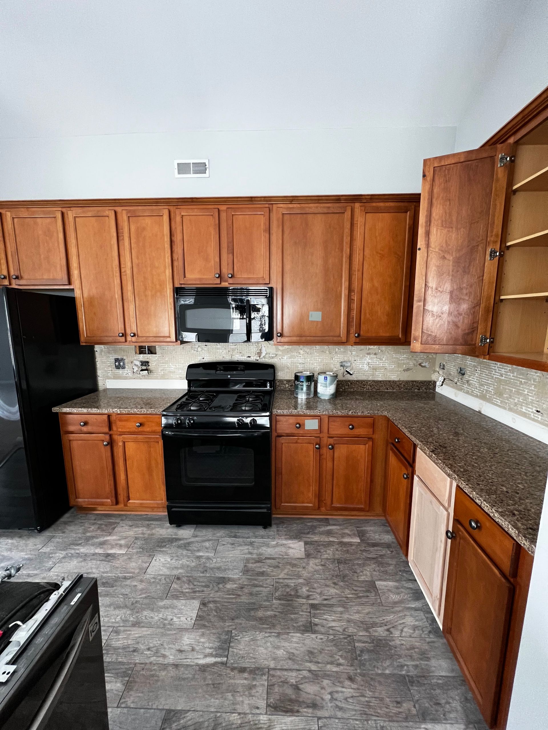 Kitchen with wooden cabinets, black stove and fridge, granite countertops, and gray tile floor.