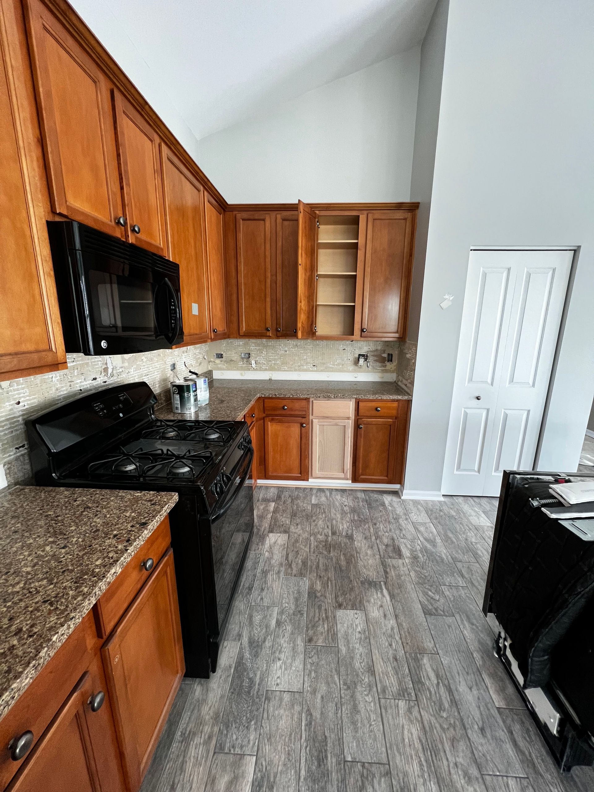 Small kitchen with wood cabinets, black appliances, speckled countertops, and gray wood-look flooring.