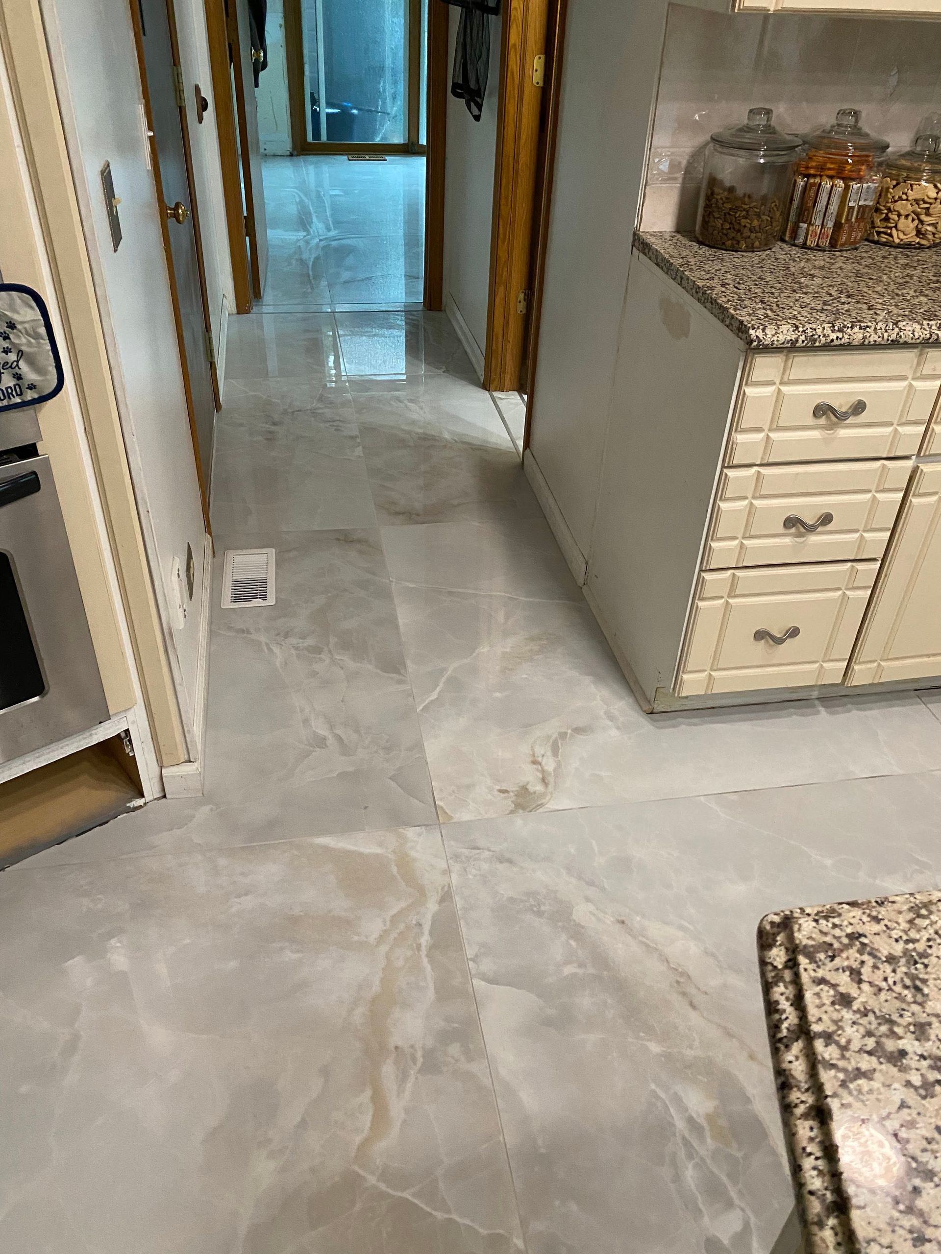 Kitchen hallway with light stone tile floor, white cabinets, and granite countertops.