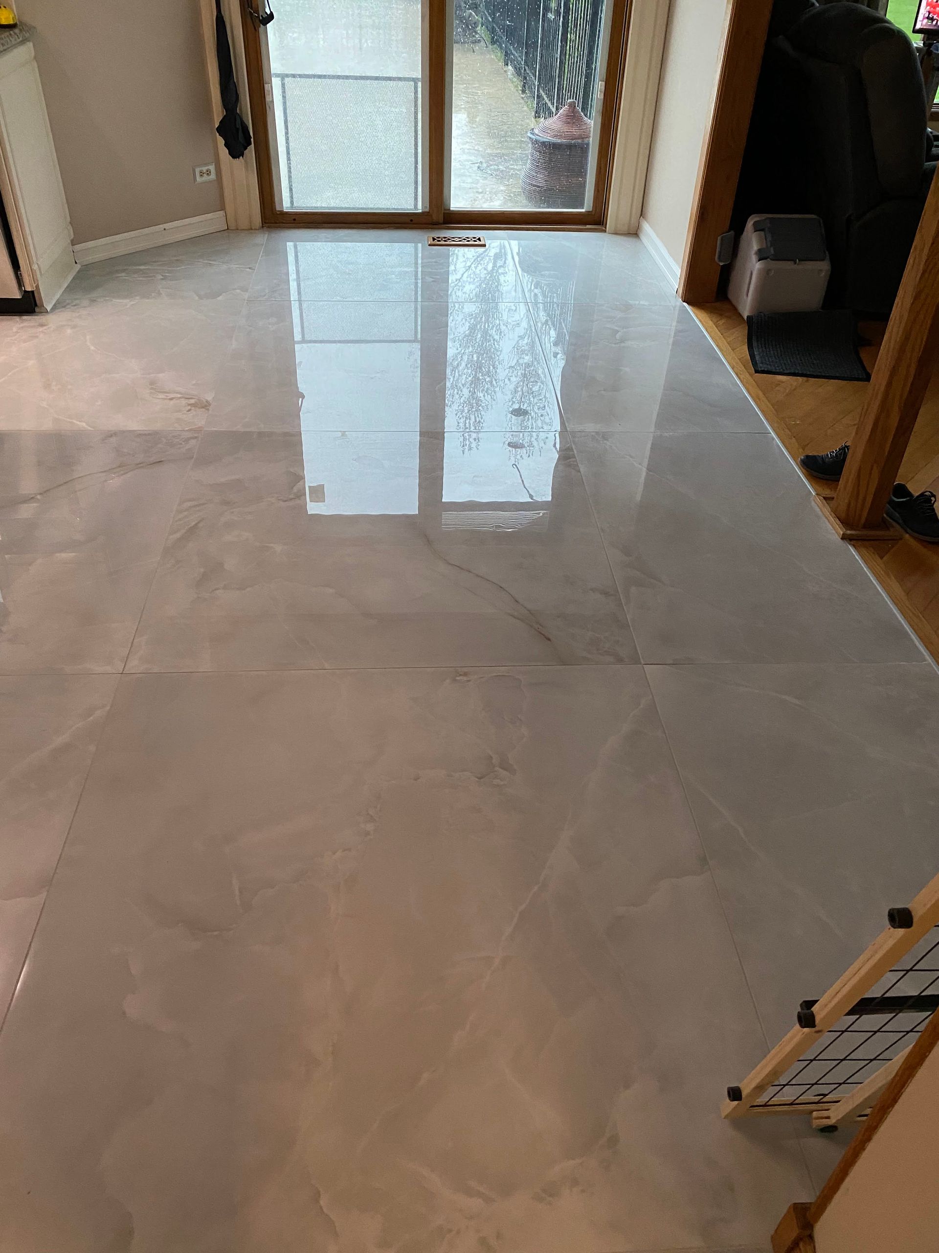 Glossy tiled floor in a hallway, reflecting light from glass doors at the end.
