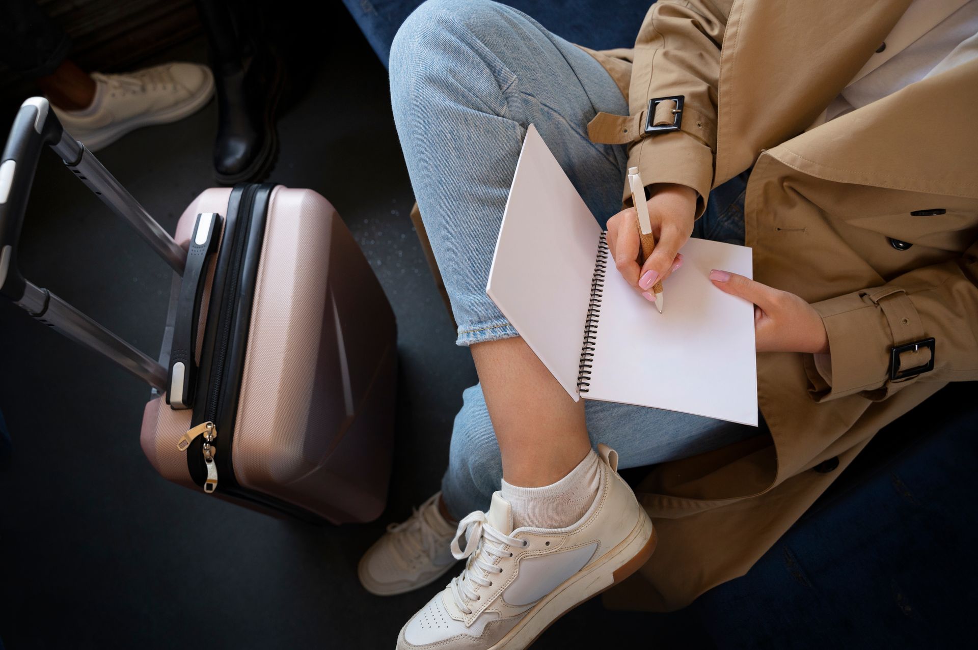 Persona escribiendo en un cuaderno en un tren, al lado de una maleta.