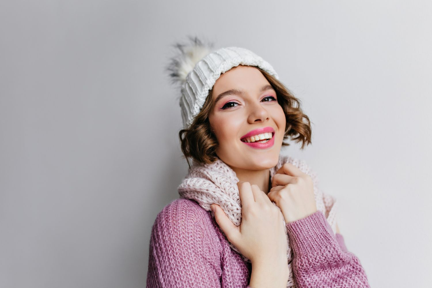 A woman wearing a hat and scarf is smiling.