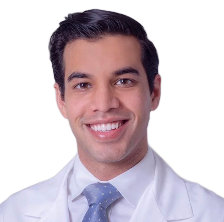 Man in a white coat smiling, wearing a blue tie, against a white background.