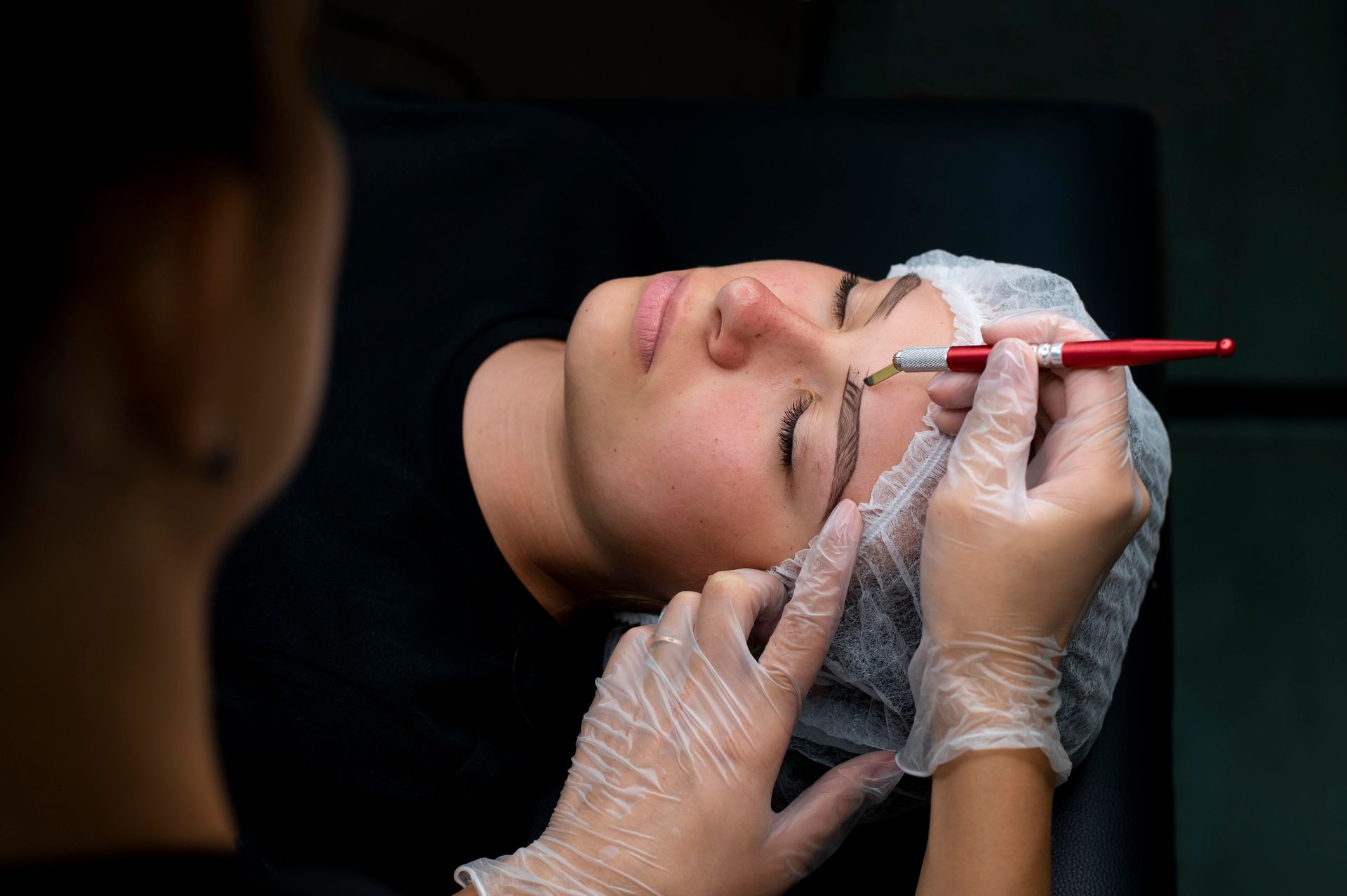 A woman is getting her eyebrows tattooed in a beauty salon.