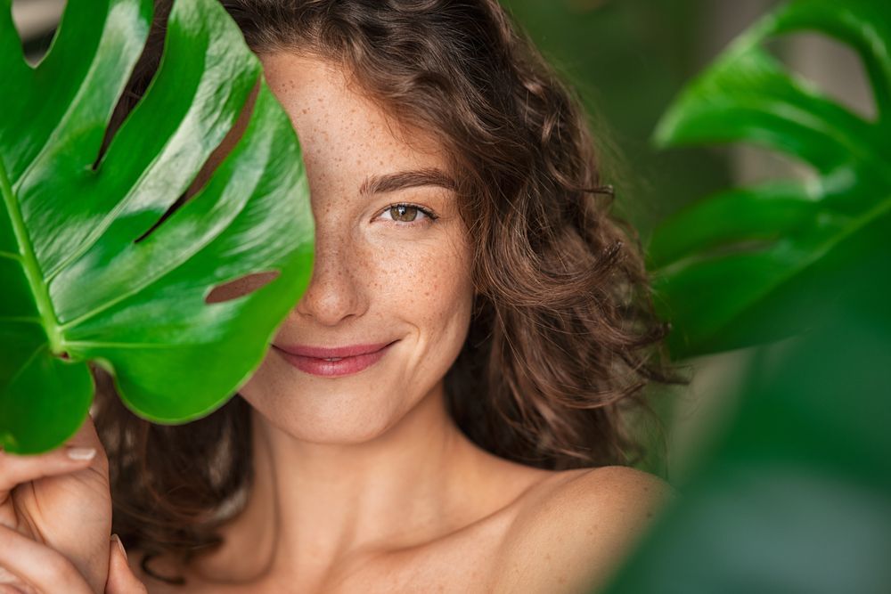 A woman is covering her face with a green leaf.