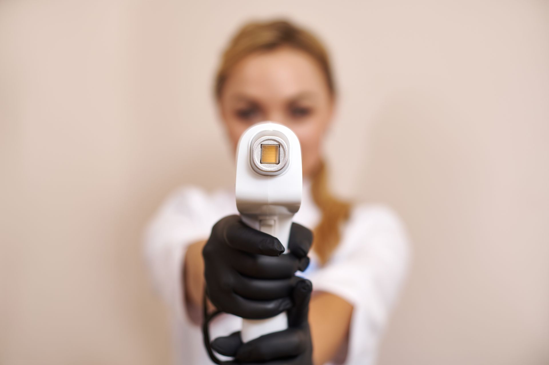 Woman holding a skin treatment device, black gloves, focused on the applicator, blurry background.