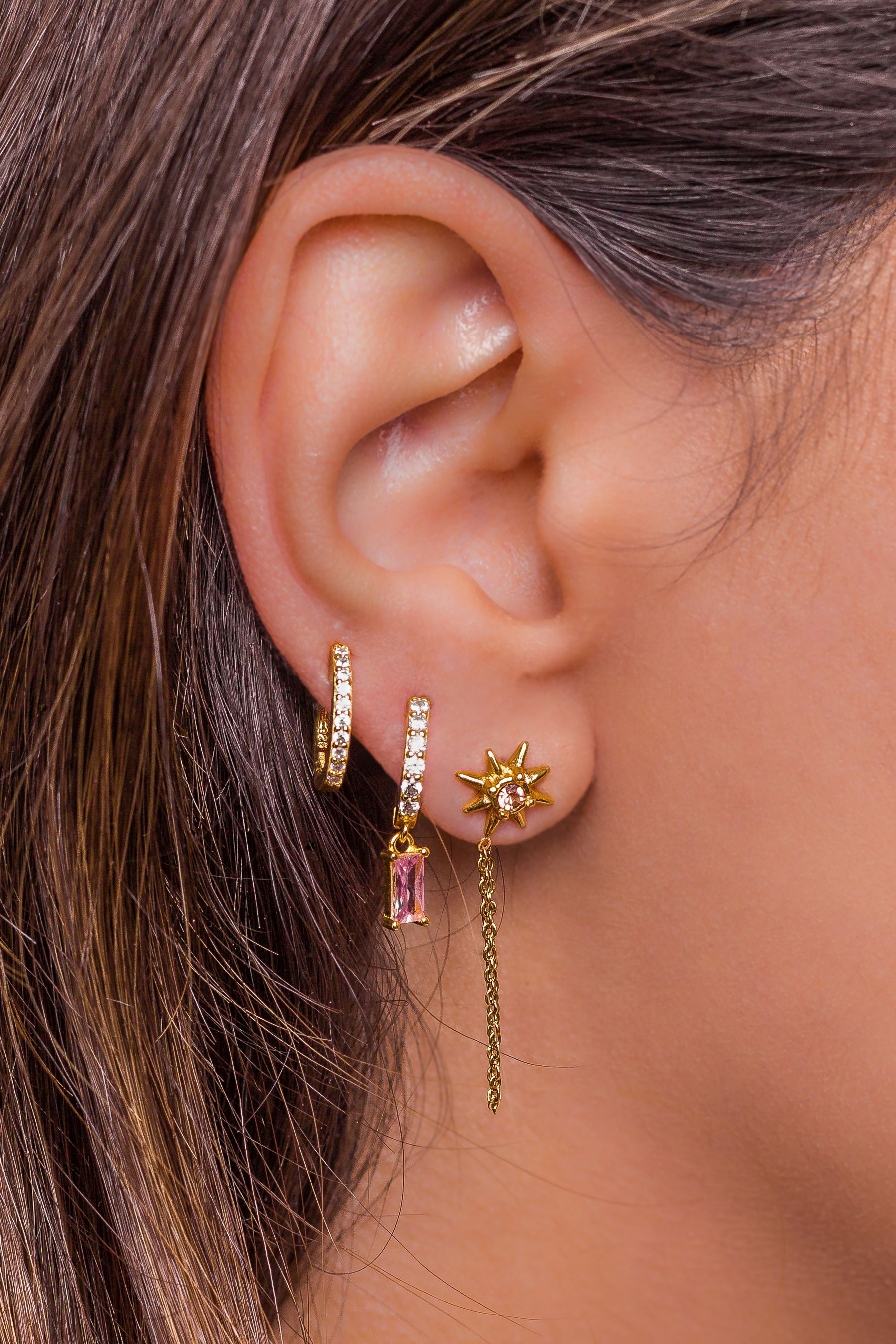 A close up of a woman 's ear with three pairs of earrings.