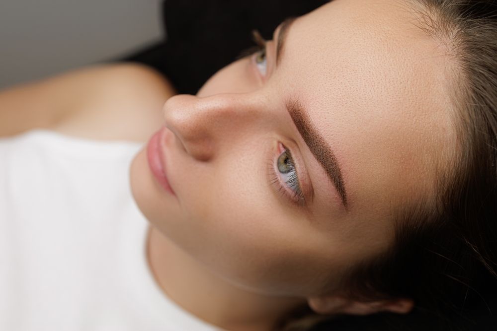 Woman with newly microbladed eyebrows, looking up with a soft expression, in a neutral setting.
