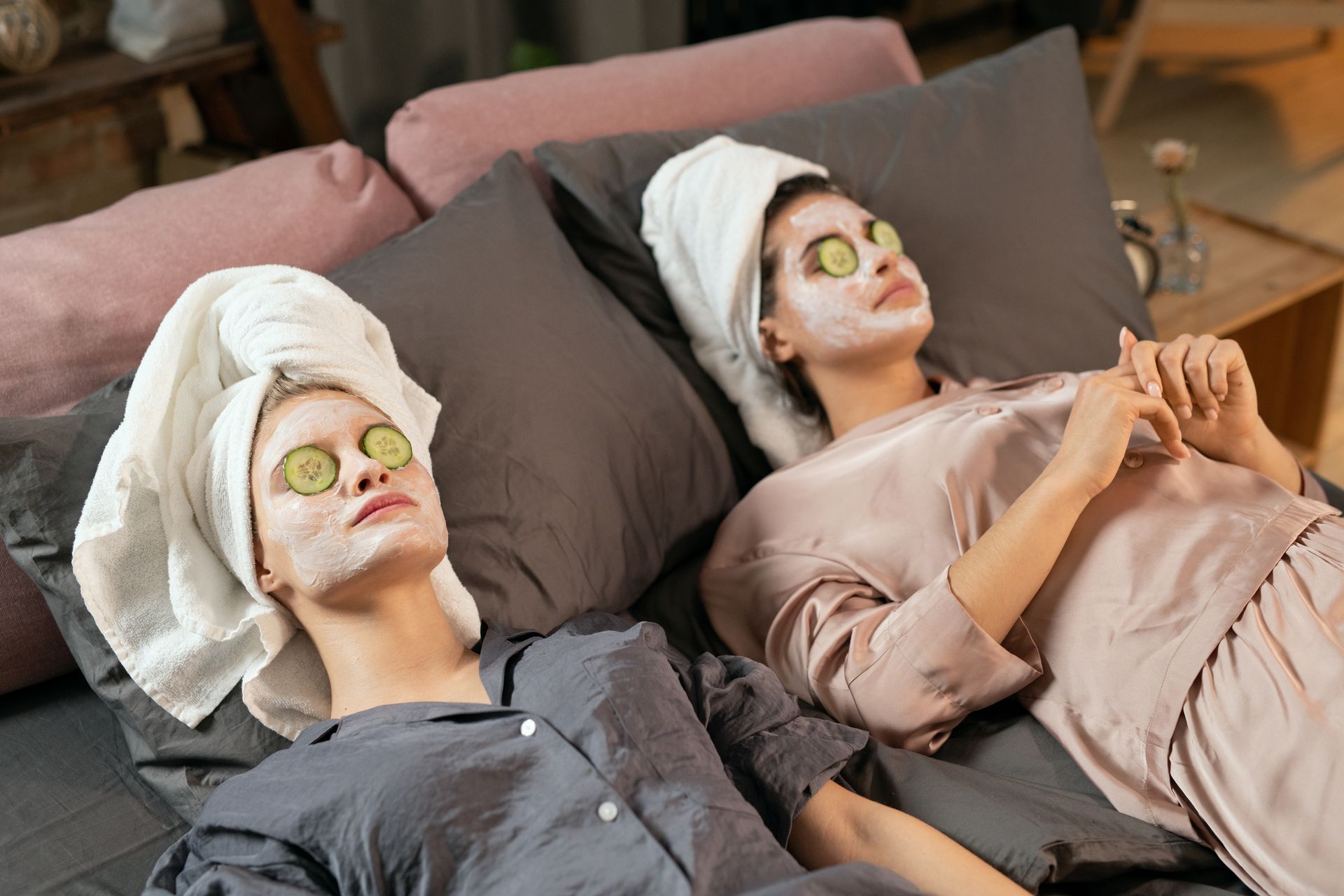 two women are laying on a couch with cucumber masks on their faces .