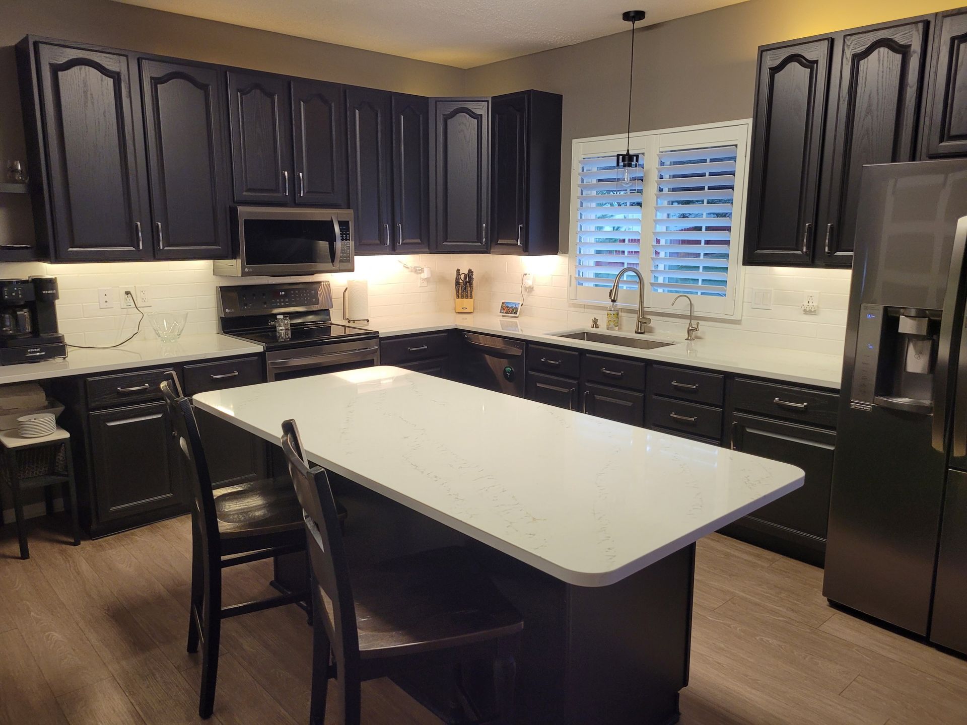 Modern kitchen with dark cabinets, white island, and stainless steel appliances around a window over the sink