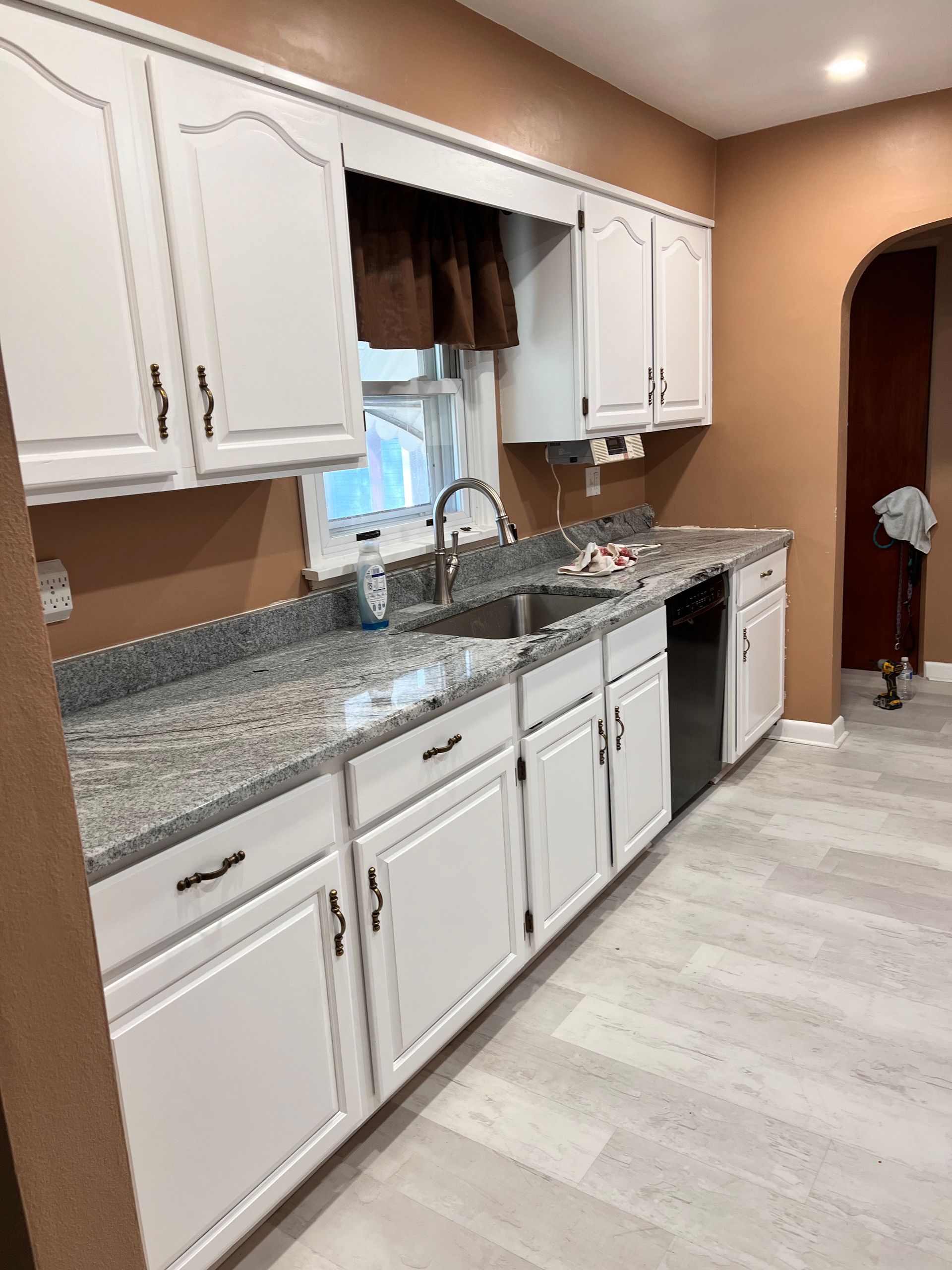 White kitchen cabinets with gray countertops, stainless steel sink, and light wood-look flooring.