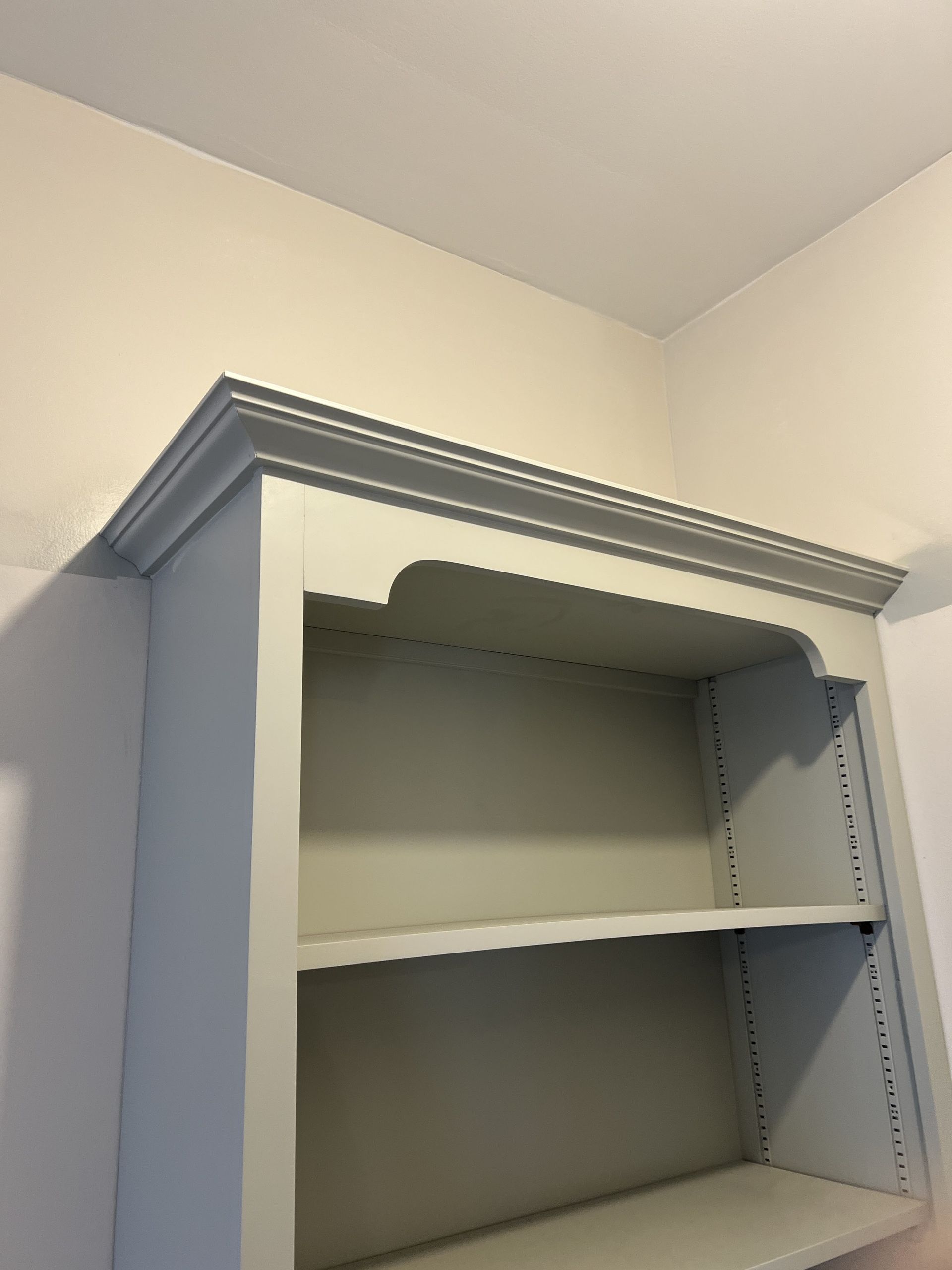 Built-in bookshelf, pale blue-gray, with two shelves. White ceiling and wall.