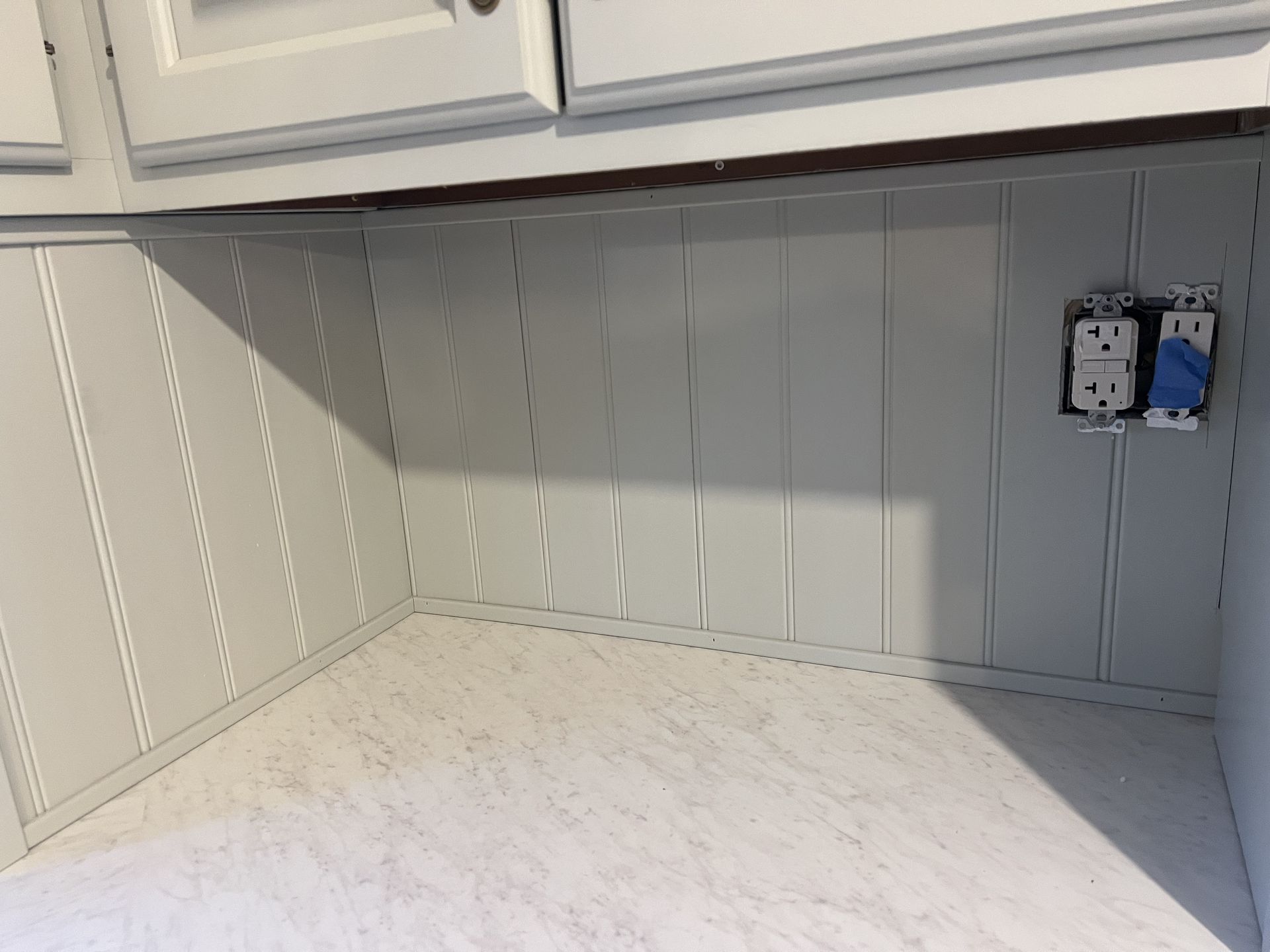White kitchen backsplash with beadboard and electrical outlets.