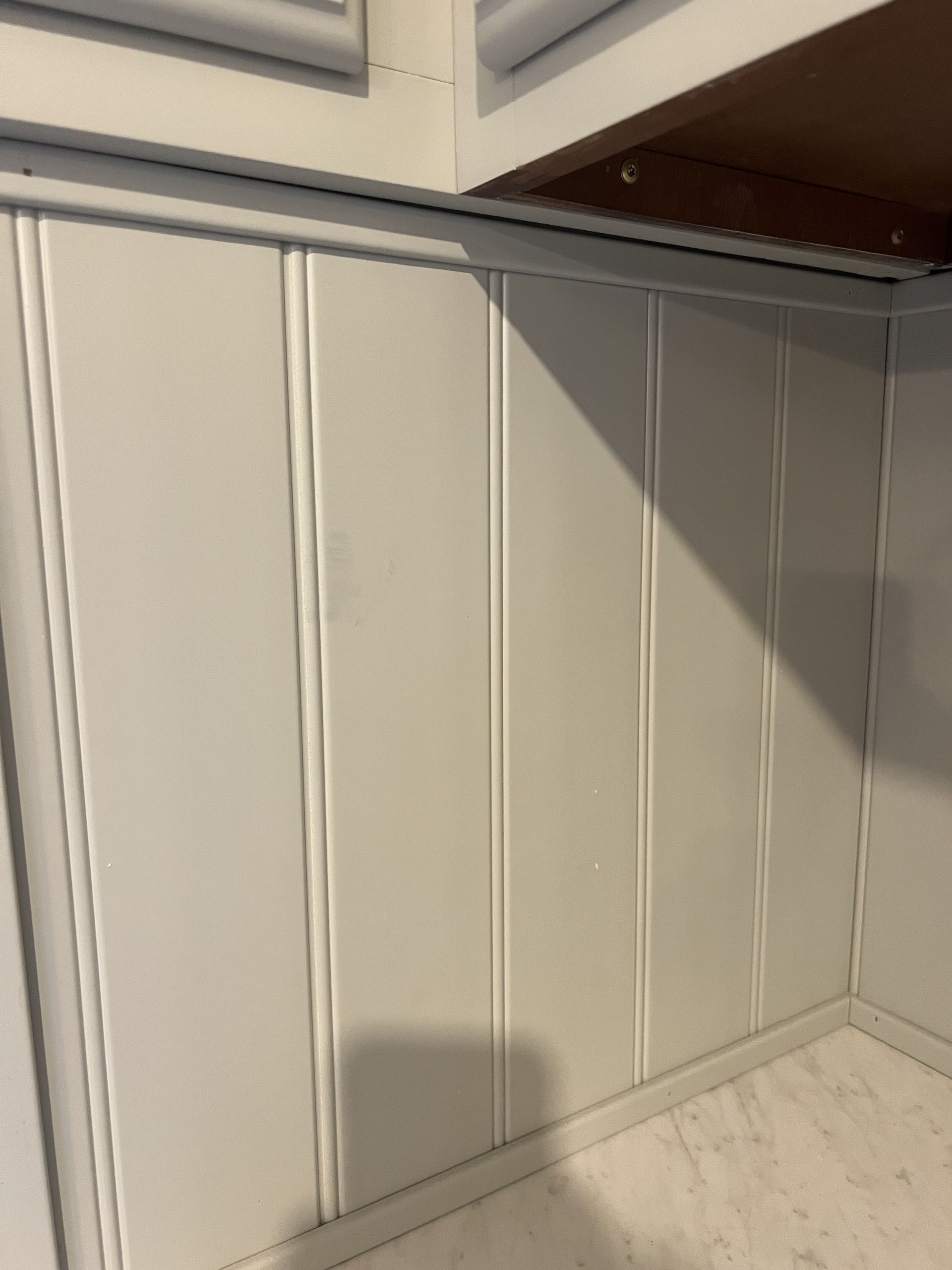 White paneled wall with vertical grooves, in a corner.