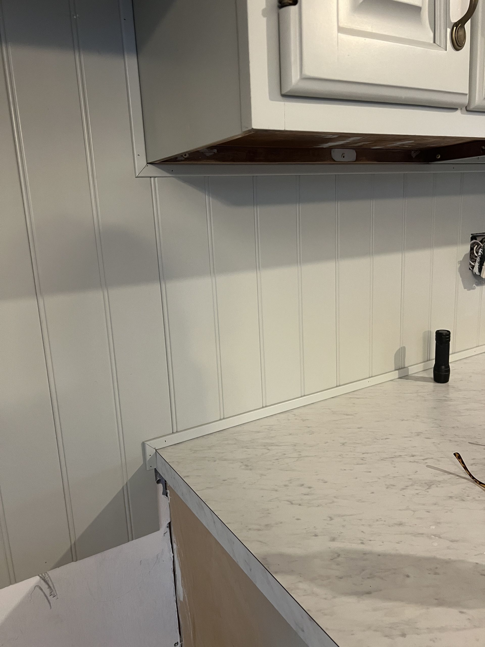 White kitchen with beadboard backsplash, white cabinets, and light countertop.