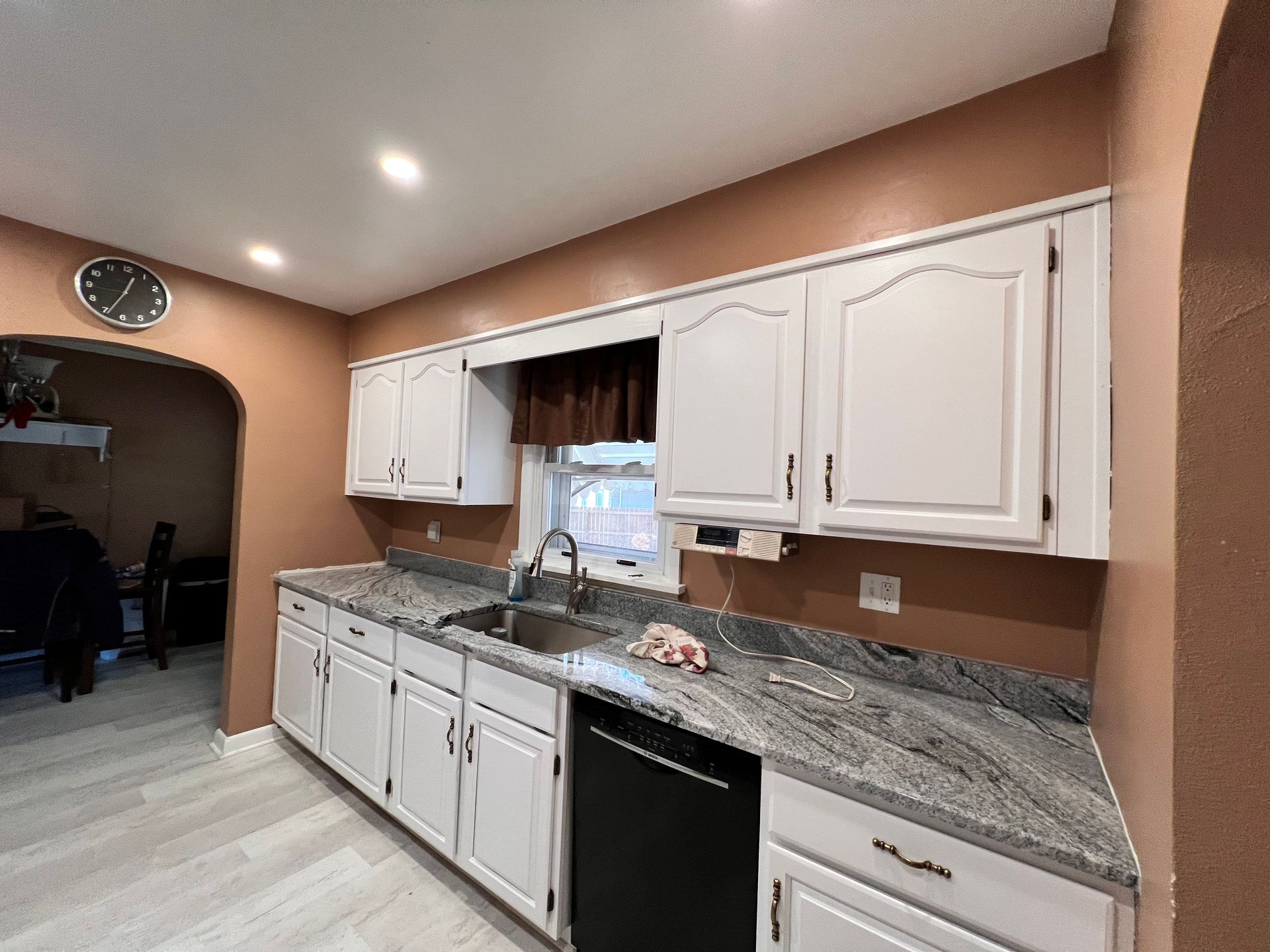 Kitchen with white cabinets, gray countertop, black appliances, and brown walls.