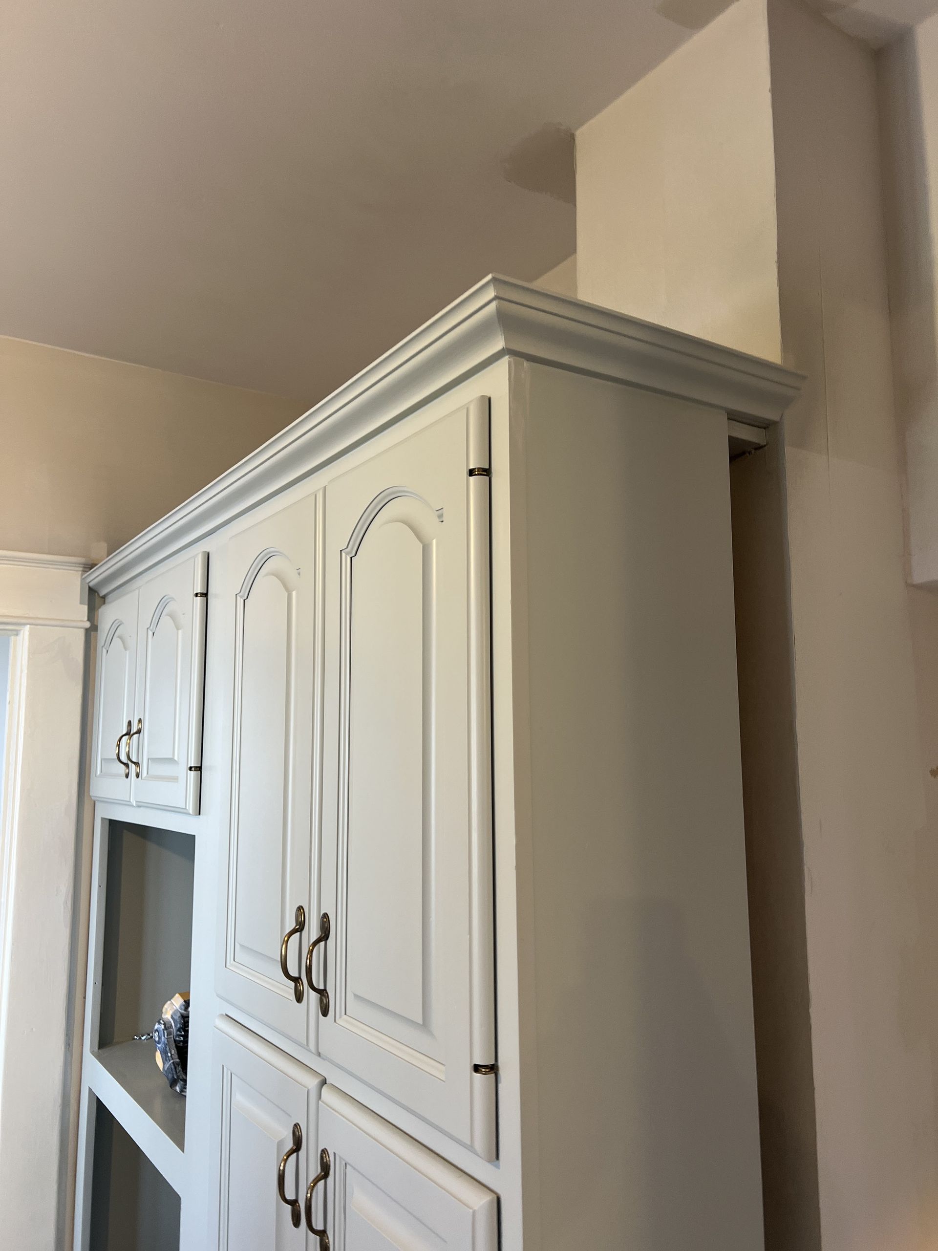 White kitchen cabinets with decorative molding against a beige wall.