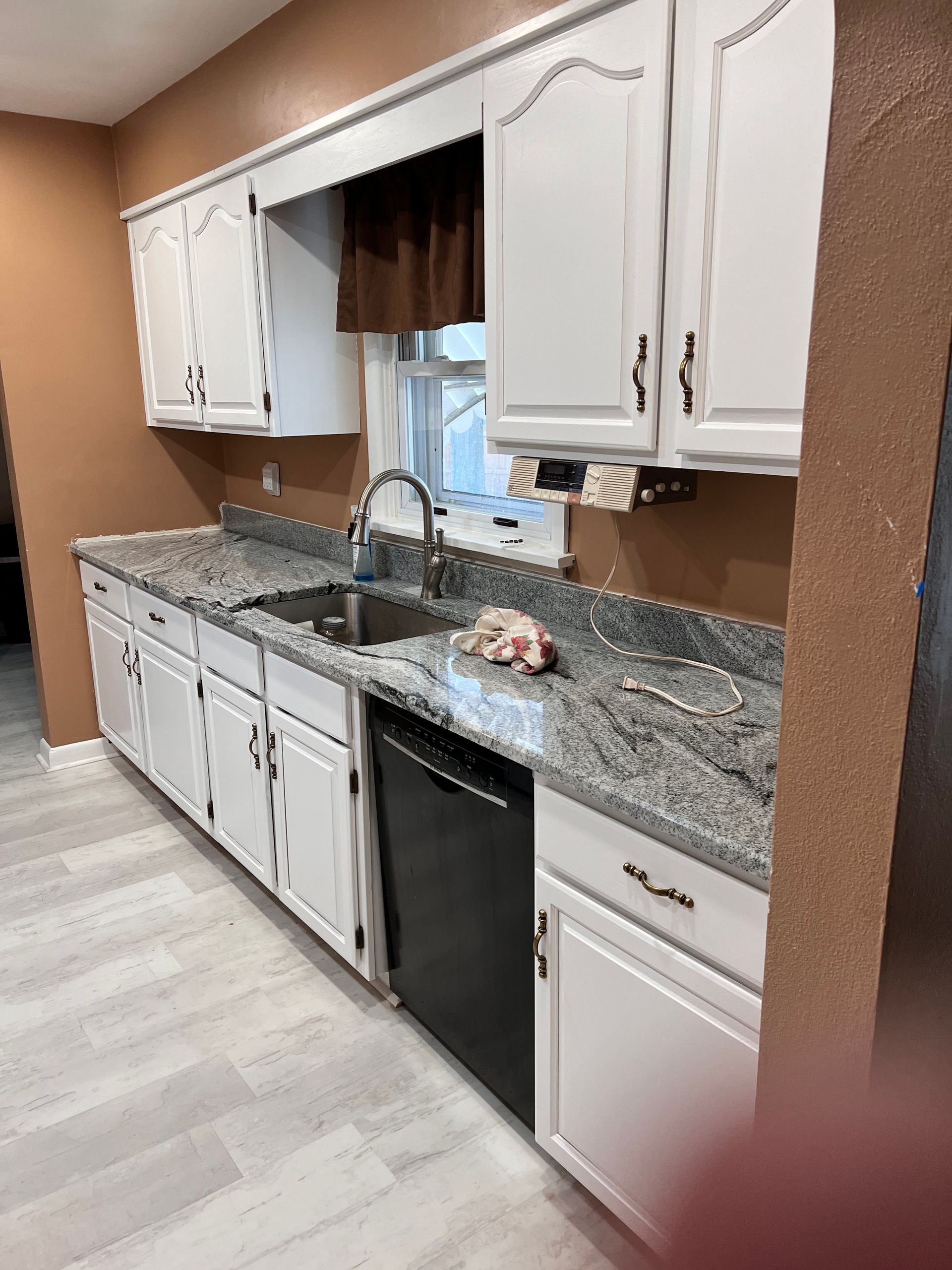 White kitchen cabinets with granite countertops, stainless steel sink and black dishwasher.