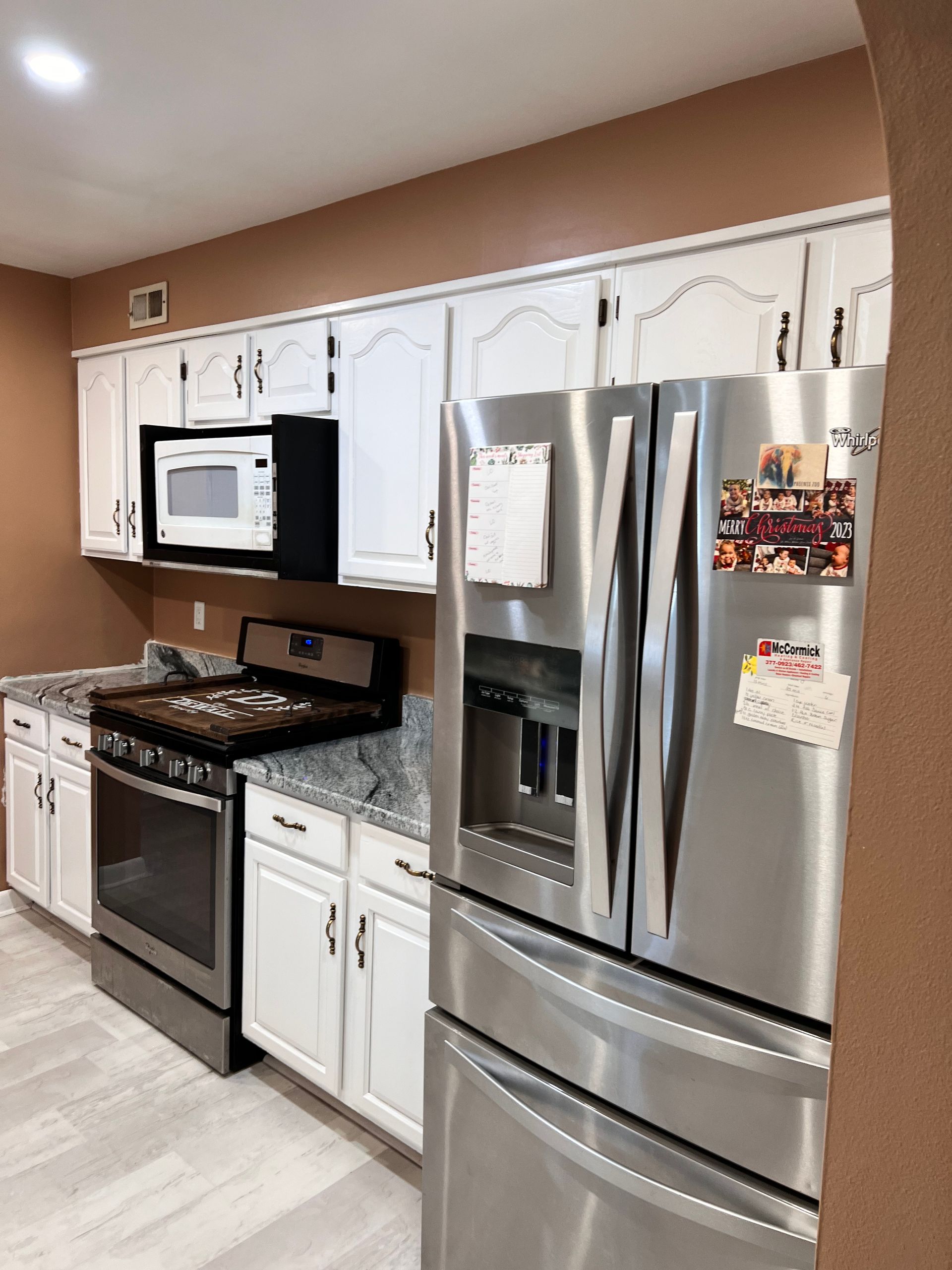 White kitchen cabinets, stainless steel refrigerator, and oven in a kitchen with brown walls.