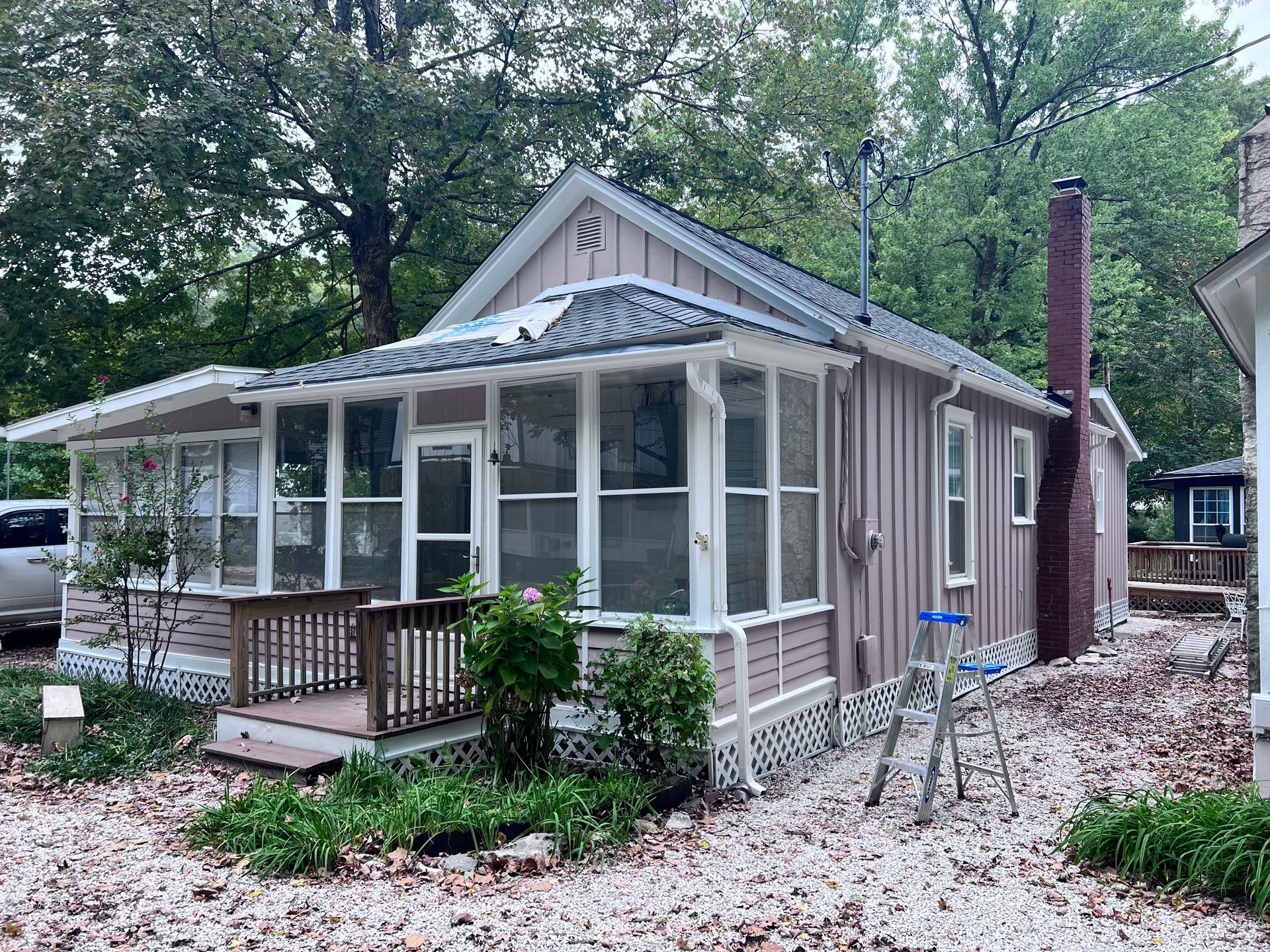 Pink-sided cottage with screened porch, dark roof, chimney, small front deck, and stone yard.