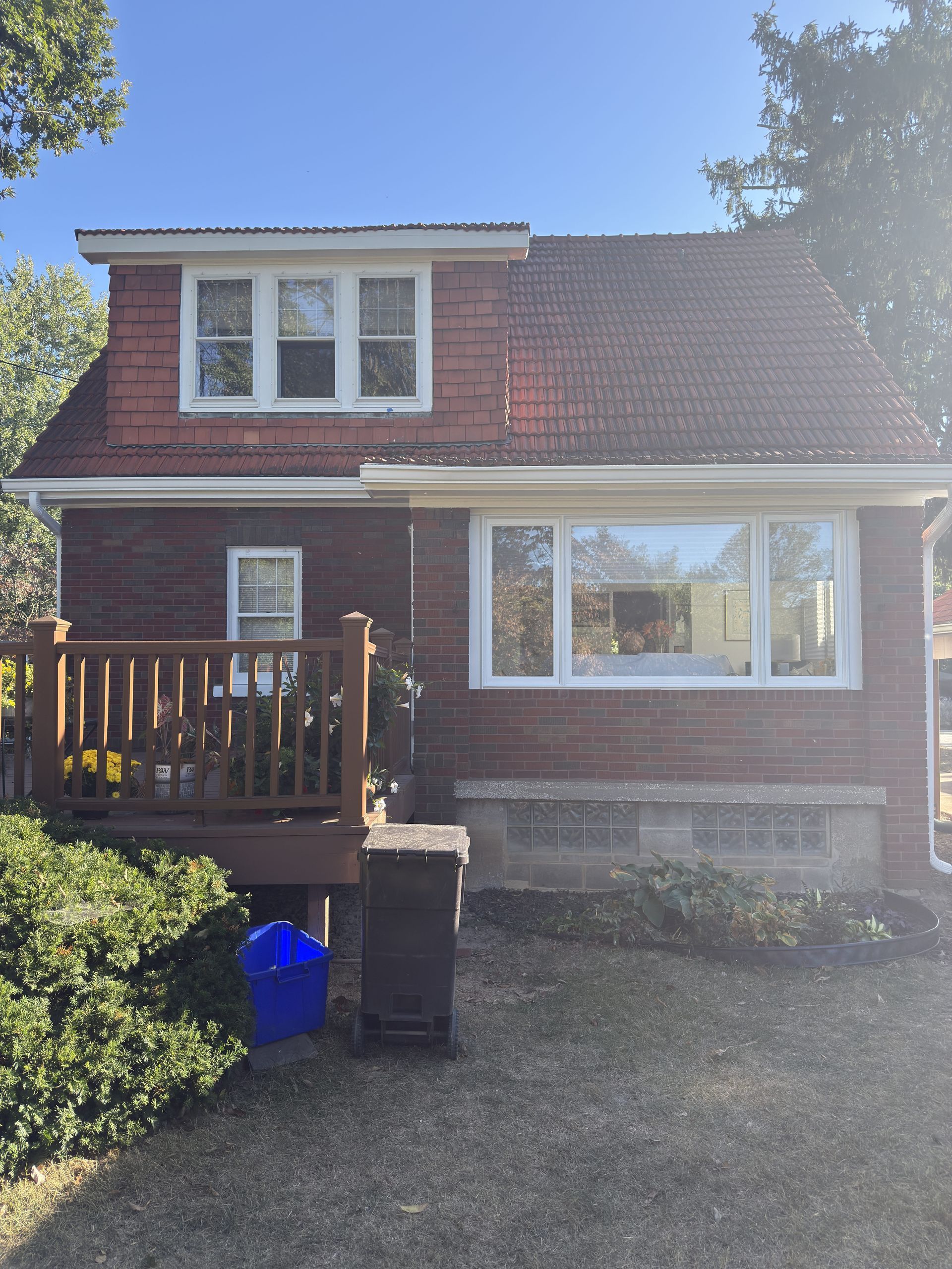 Red brick house with a deck, windows, and a blue bin on the lawn.