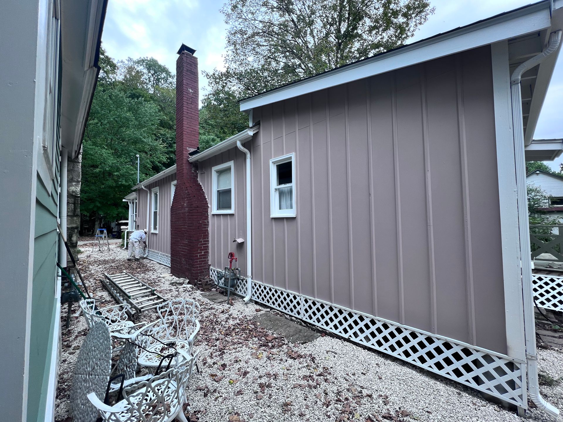 Side view of a beige-sided house with a red brick chimney, white trim, and a latticed foundation skirt.