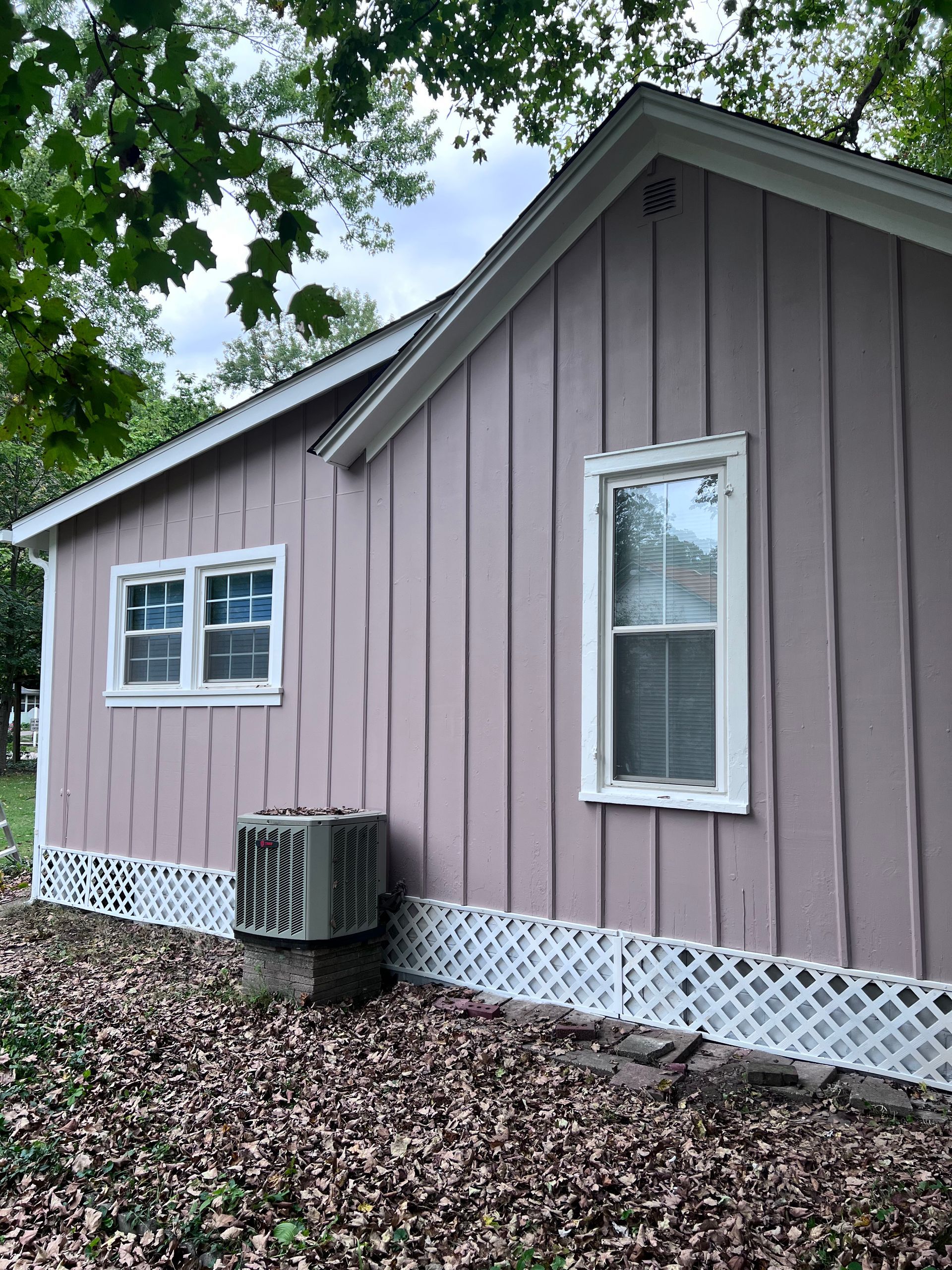 Side view of a pink house with white trim, windows, and lattice skirting. An air conditioning unit sits below.