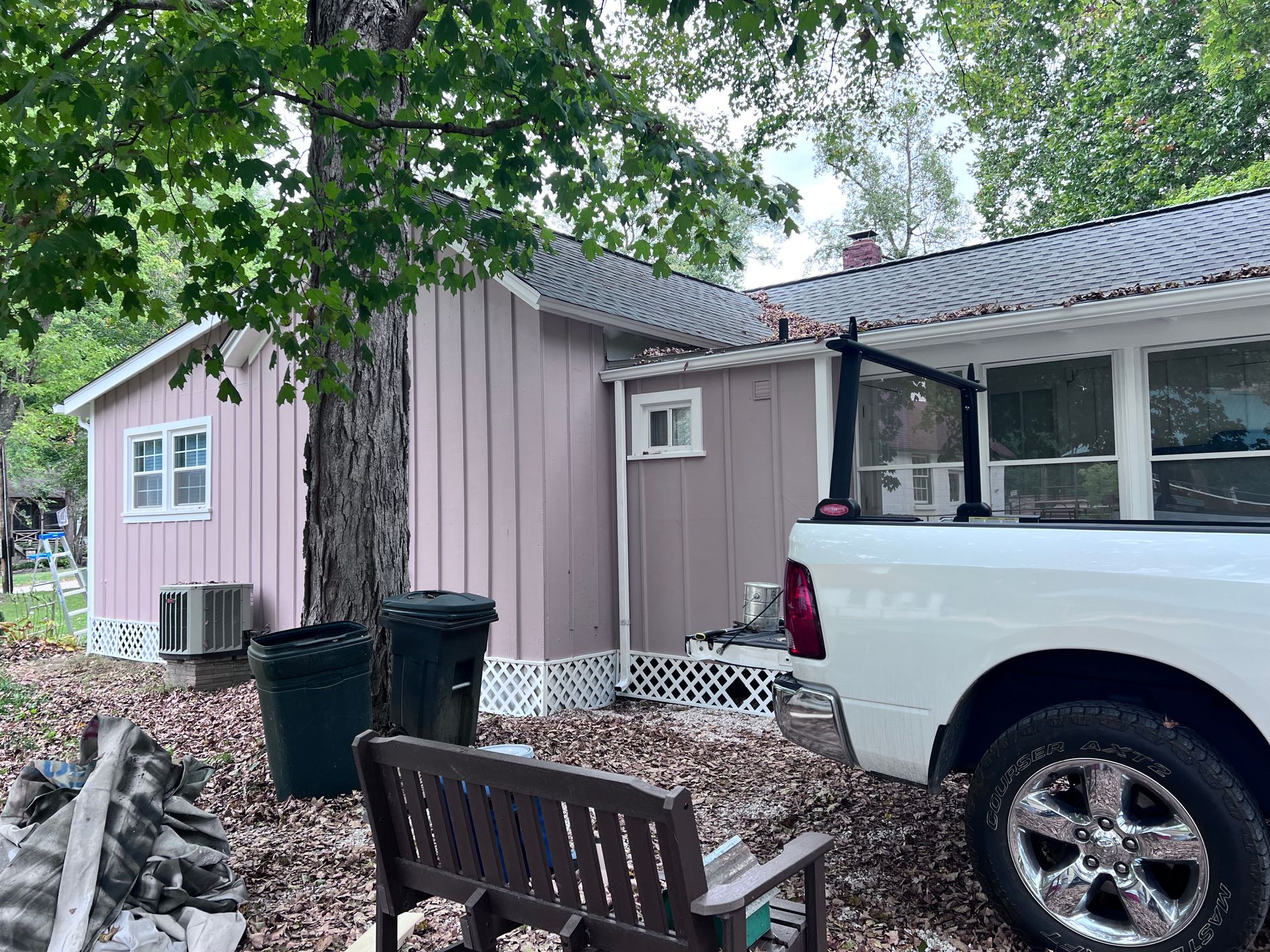Pink house with white trim; white truck parked beside it. Tree, trash cans, bench in front.