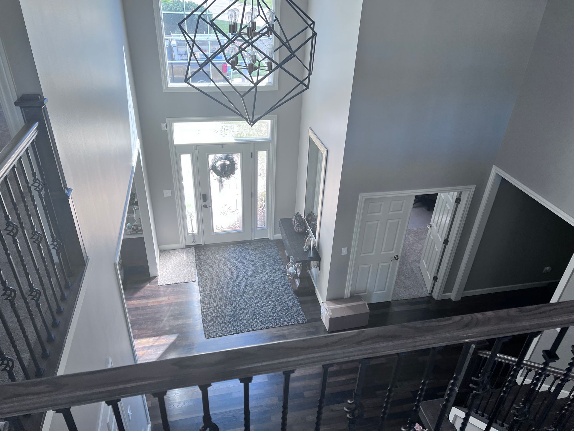 View from a stairway landing of a home's entryway with dark wood floors, gray walls, and a decorative light fixture.