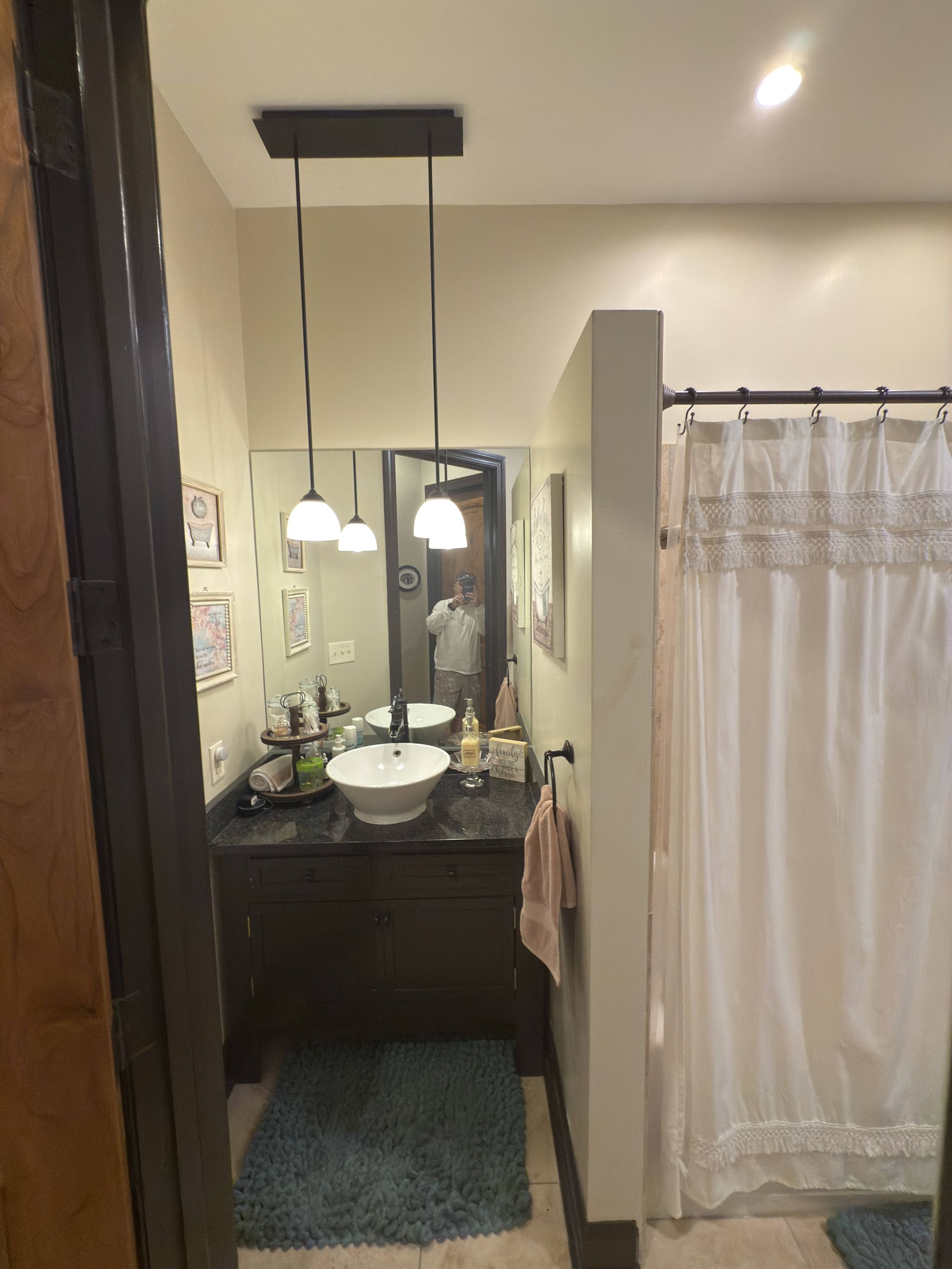 Bathroom with dark vanity, white sink, and decorative lighting. Shower with curtain on the right.