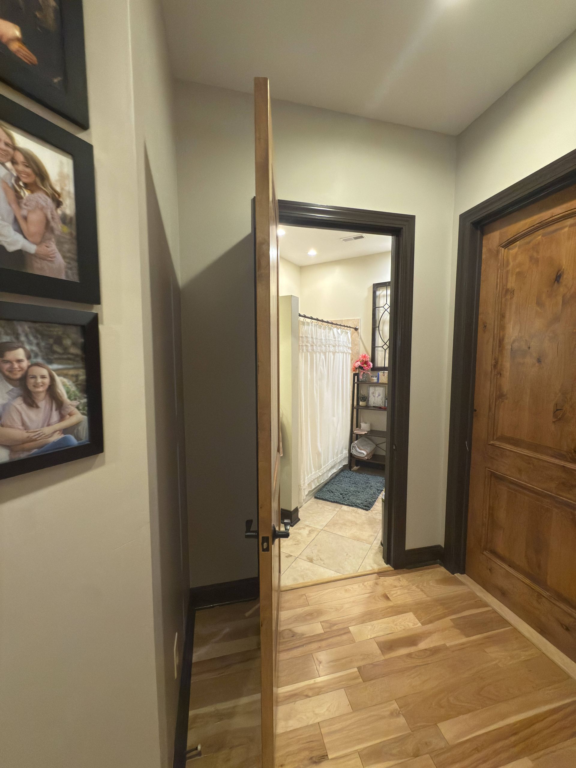 Hallway with open door to bathroom, wooden floor and doors, framed photos on wall.