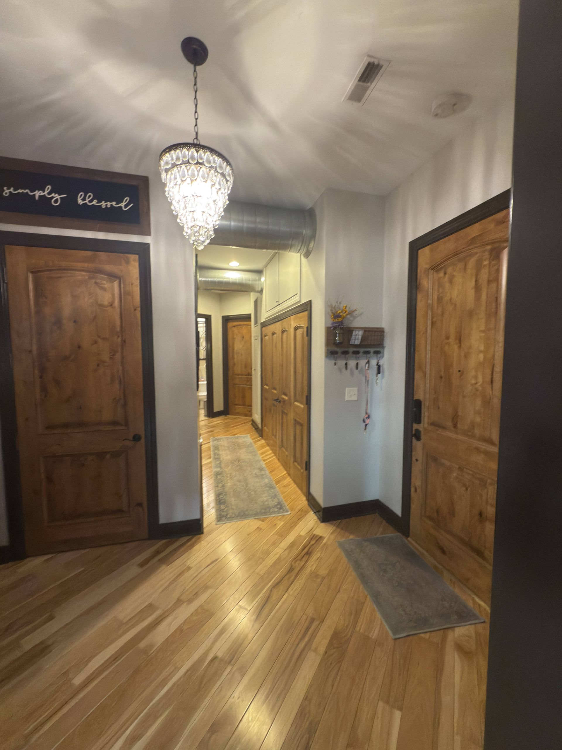 Hallway with wooden doors and floors. A crystal chandelier hangs from the ceiling.