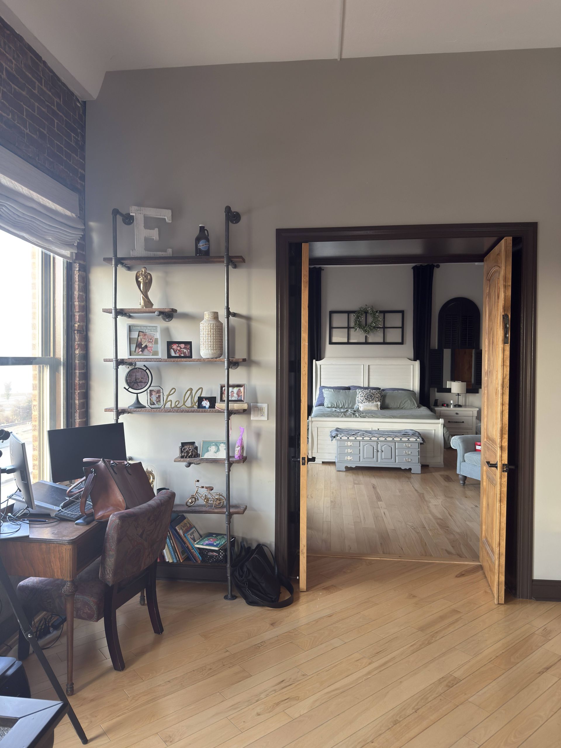 Room interior: home office with desk, shelving, and doorway to bedroom with bed.