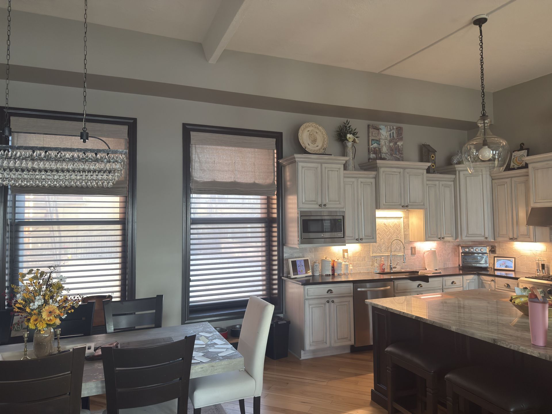 Kitchen with white cabinets, island, and dining area with shades and chandeliers.