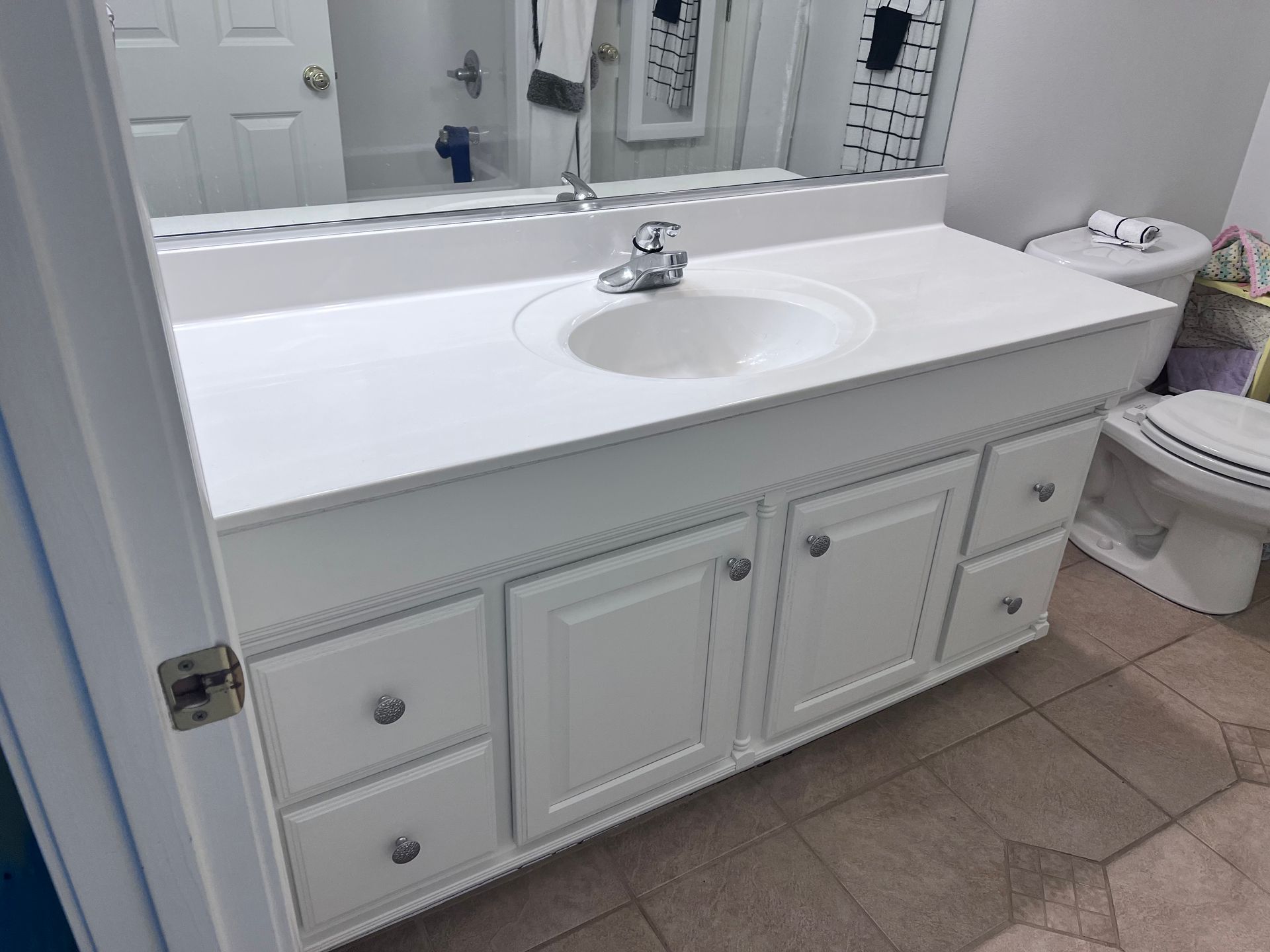 White bathroom vanity with sink and cabinets, next to a toilet.