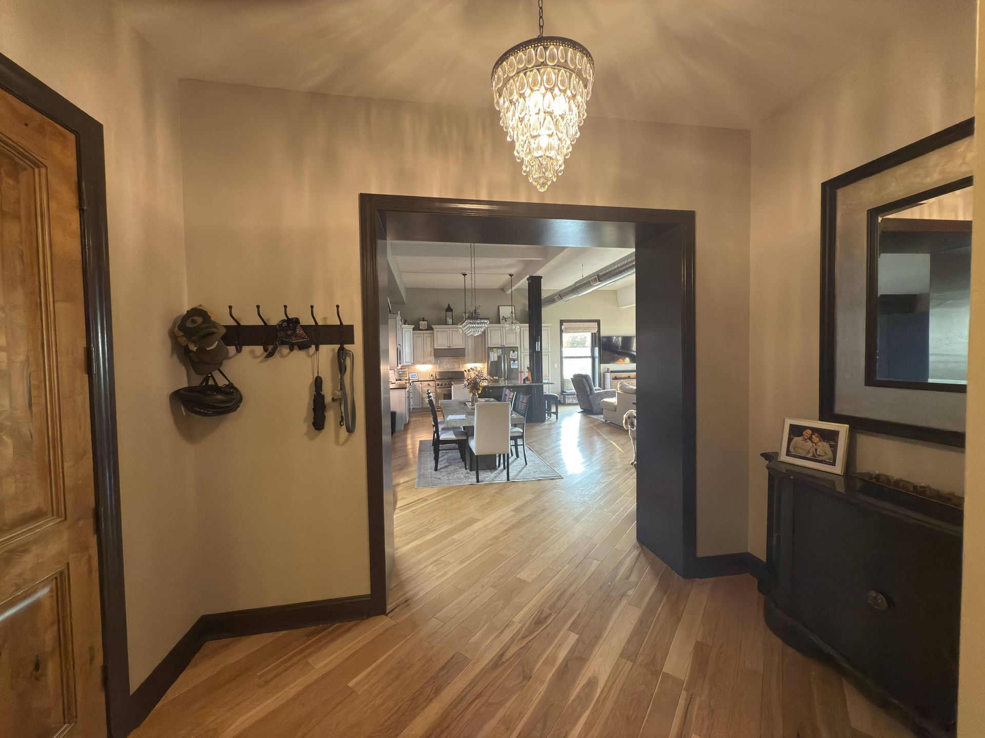 Hallway with chandelier, wooden floor, open doorway into a living area.
