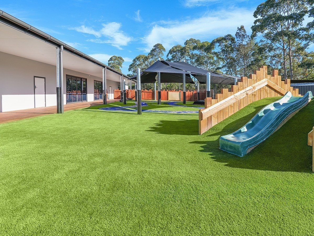 A playground with a slide and a wooden ramp in front of a building.