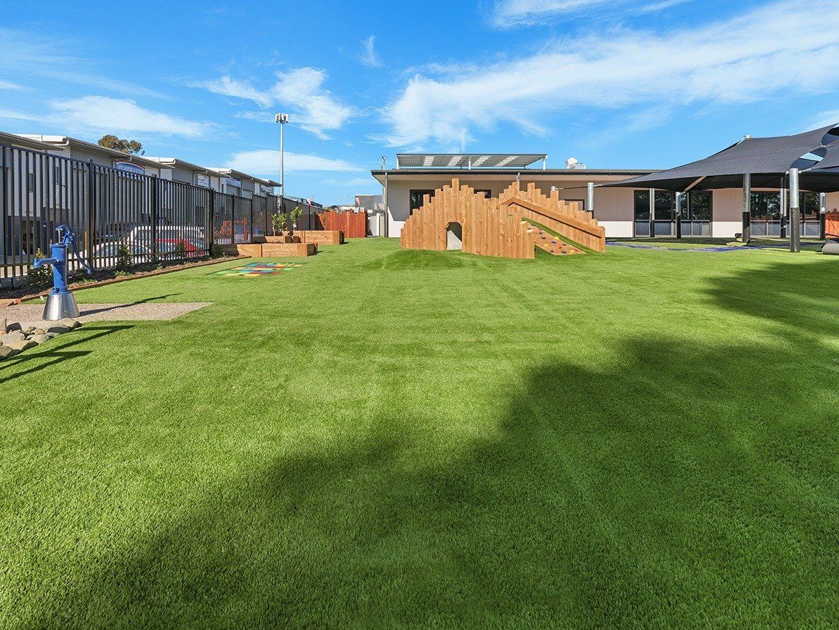 A large lawn with a wooden structure in the middle of it and a house in the background.