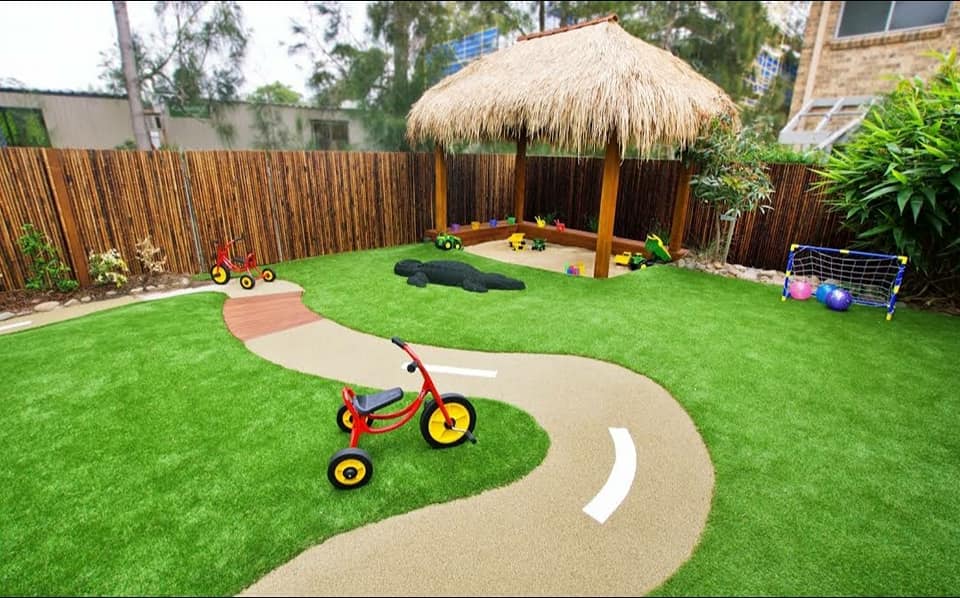 A red tricycle is sitting on the grass in a backyard.