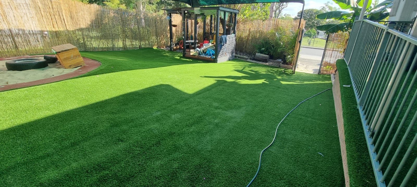 A lush green lawn with a playground in the background and a fence.