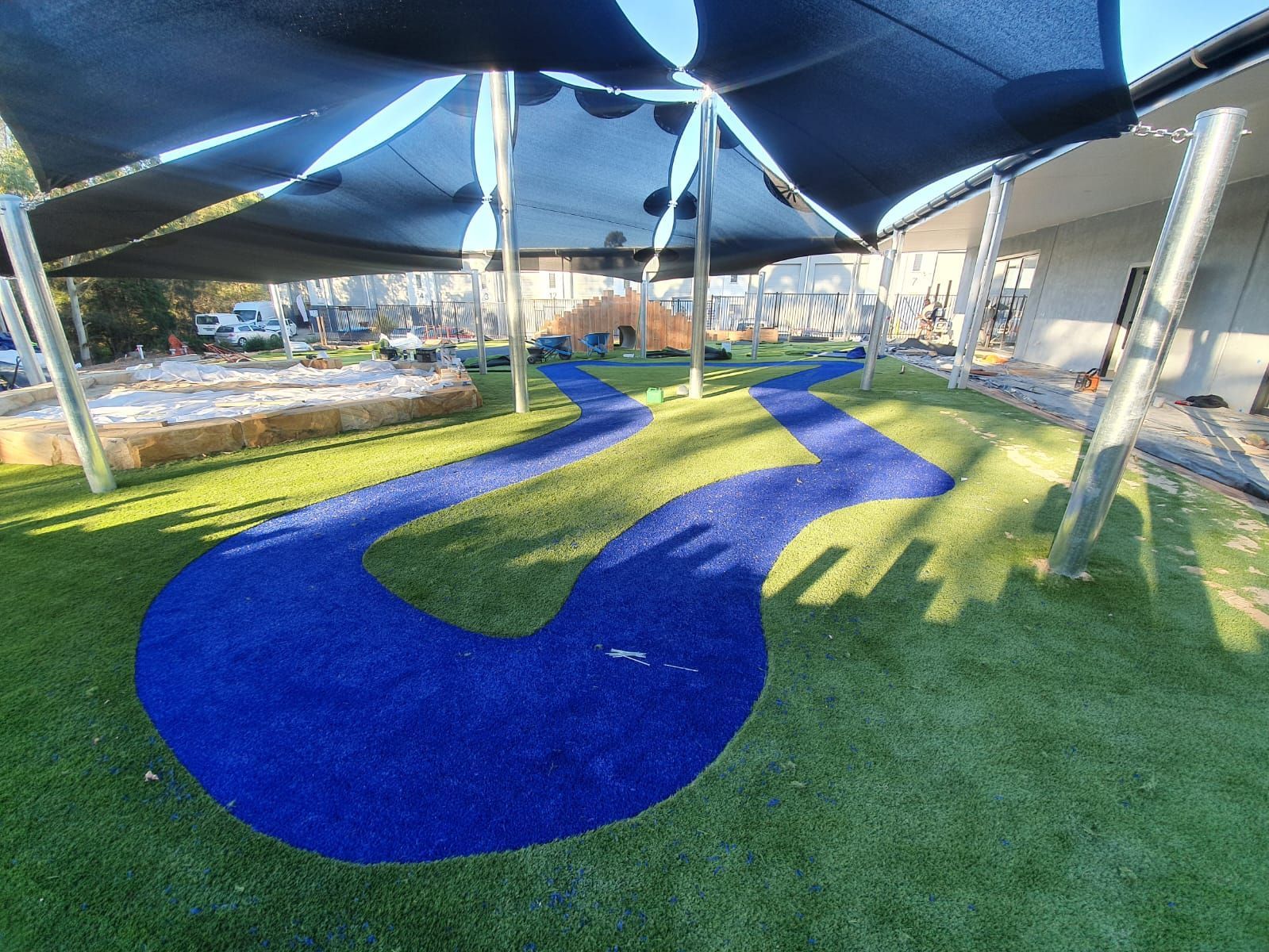 A blue path is going through the grass under a canopy.