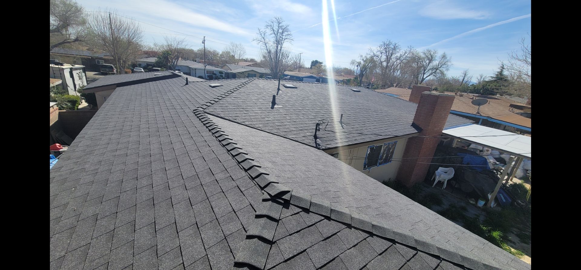 Overhead view of a house roof with dark gray shingles on a sunny day.