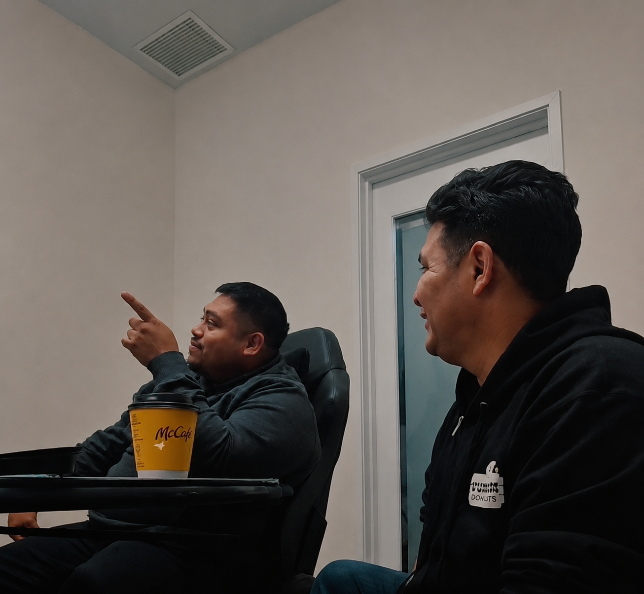 Two people seated in a room, one pointing toward the ceiling vent while the other watches.