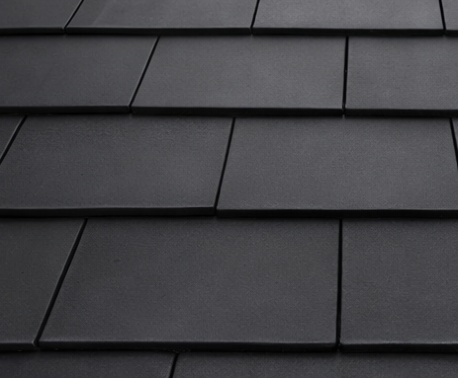 Close-up of a dark gray, textured roof tile pattern. Rectangular, overlapping tiles.