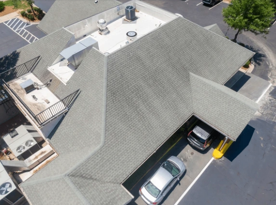Aerial view of a gray-shingled building with cars parked underneath a covered area.
