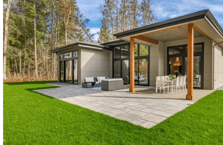 Modern home with patio, green lawn, and forest backdrop.