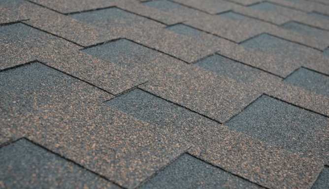 Close-up of asphalt shingles, gray and brown, overlapping in a pattern on a roof.