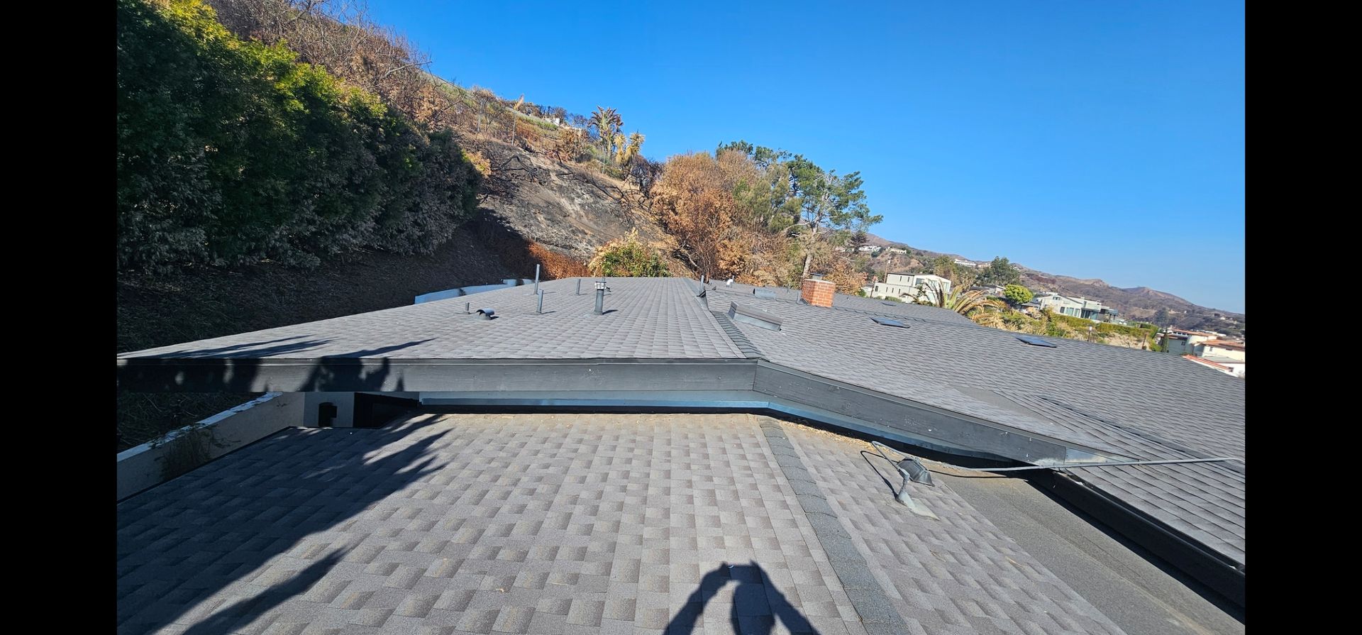 View from rooftop with gray shingles against a hillside and clear blue sky.