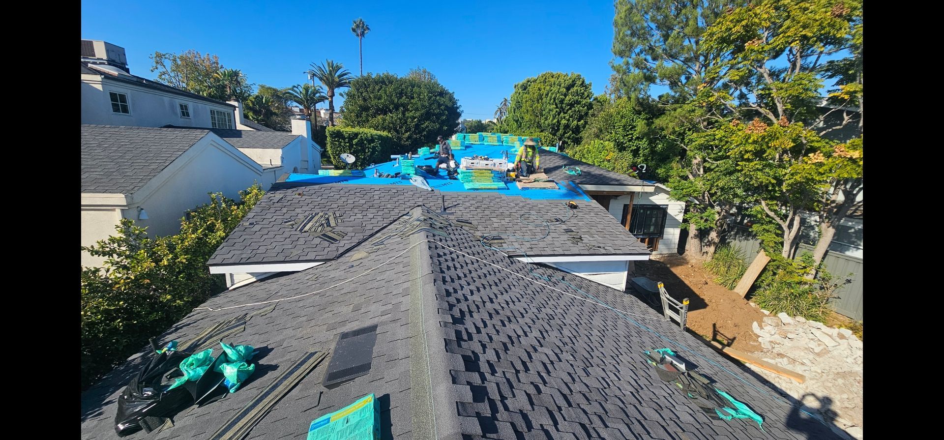 Rooftop with blue tarp and construction in progress, surrounded by trees and clear sky.