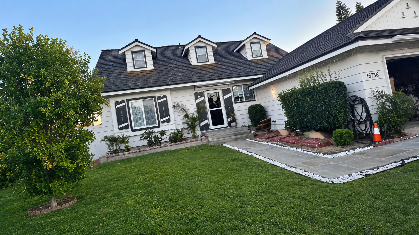 Suburban house with white siding, dark roof, front lawn, walkway, and an orange traffic cone by the entrance